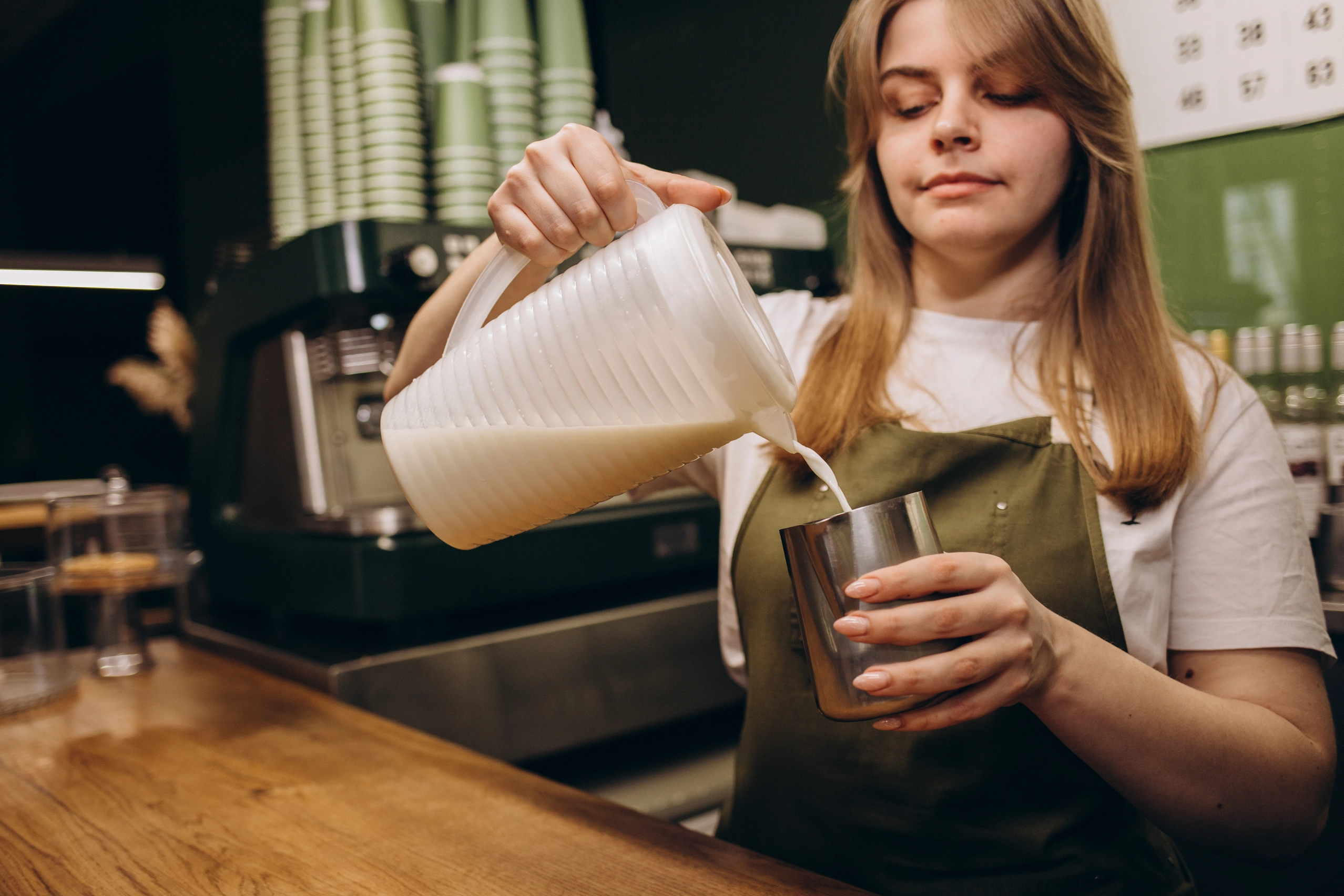 Professional female barista pouring milk into hot jug.