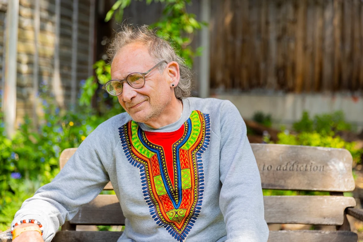 An adult Aquarius service user enjoying the garden on a wooden handmade bench.