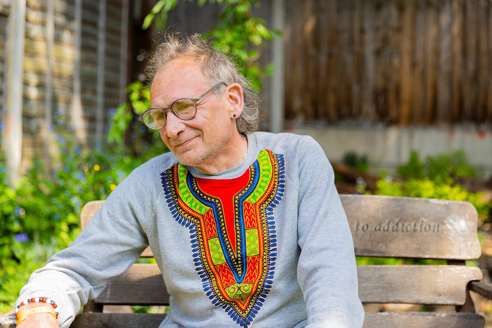 An adult Aquarius service user enjoying the garden on a wooden handmade bench.