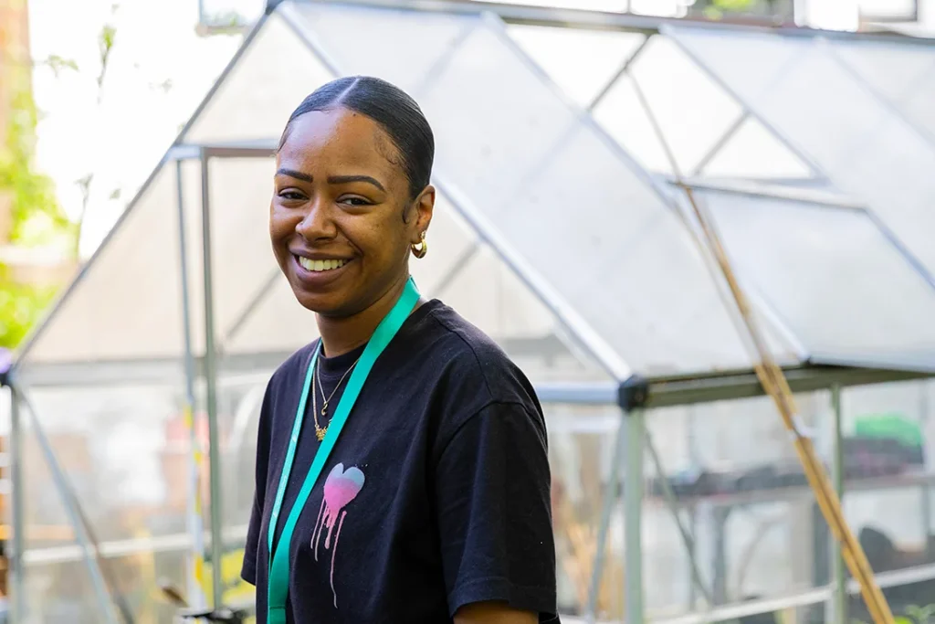 A person smiling in front of a greenhouse.