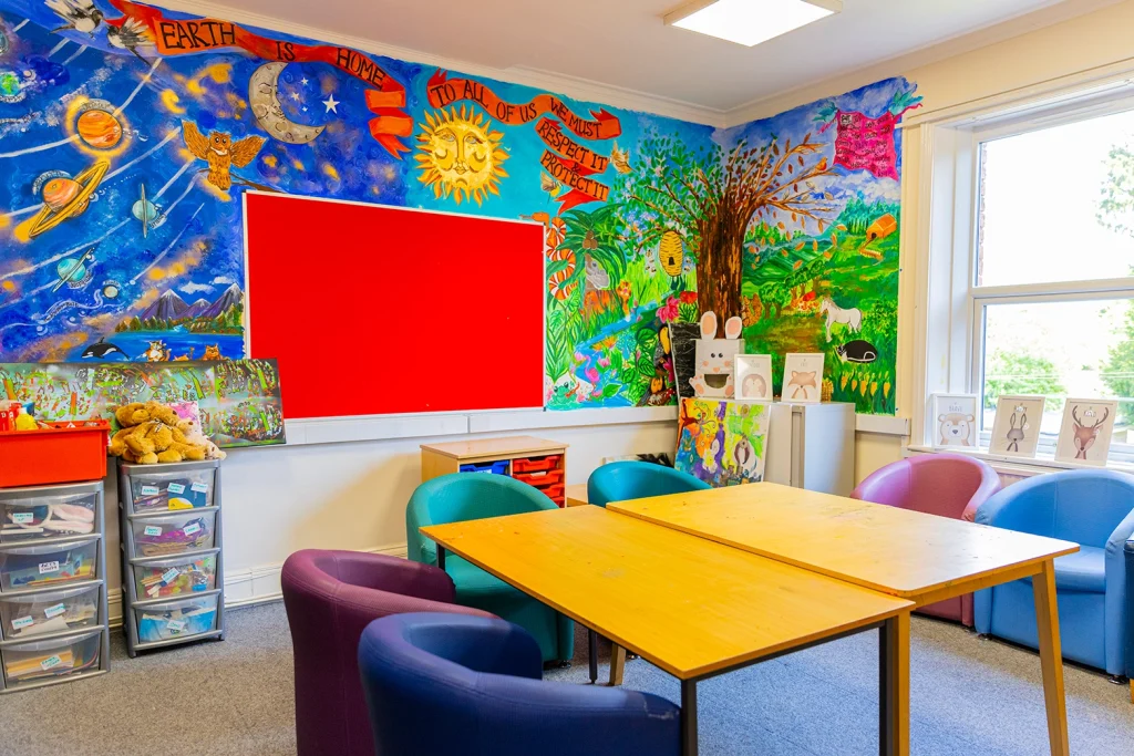 A room with soft armchairs around a table, with colourful walls.
